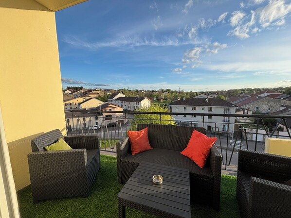 A balcony with wicker furniture, a small table, and a clear view of the surrounding neighborhood.