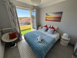 A bedroom with a bed, a view of the outside, a radiator, and a painting on the wall.