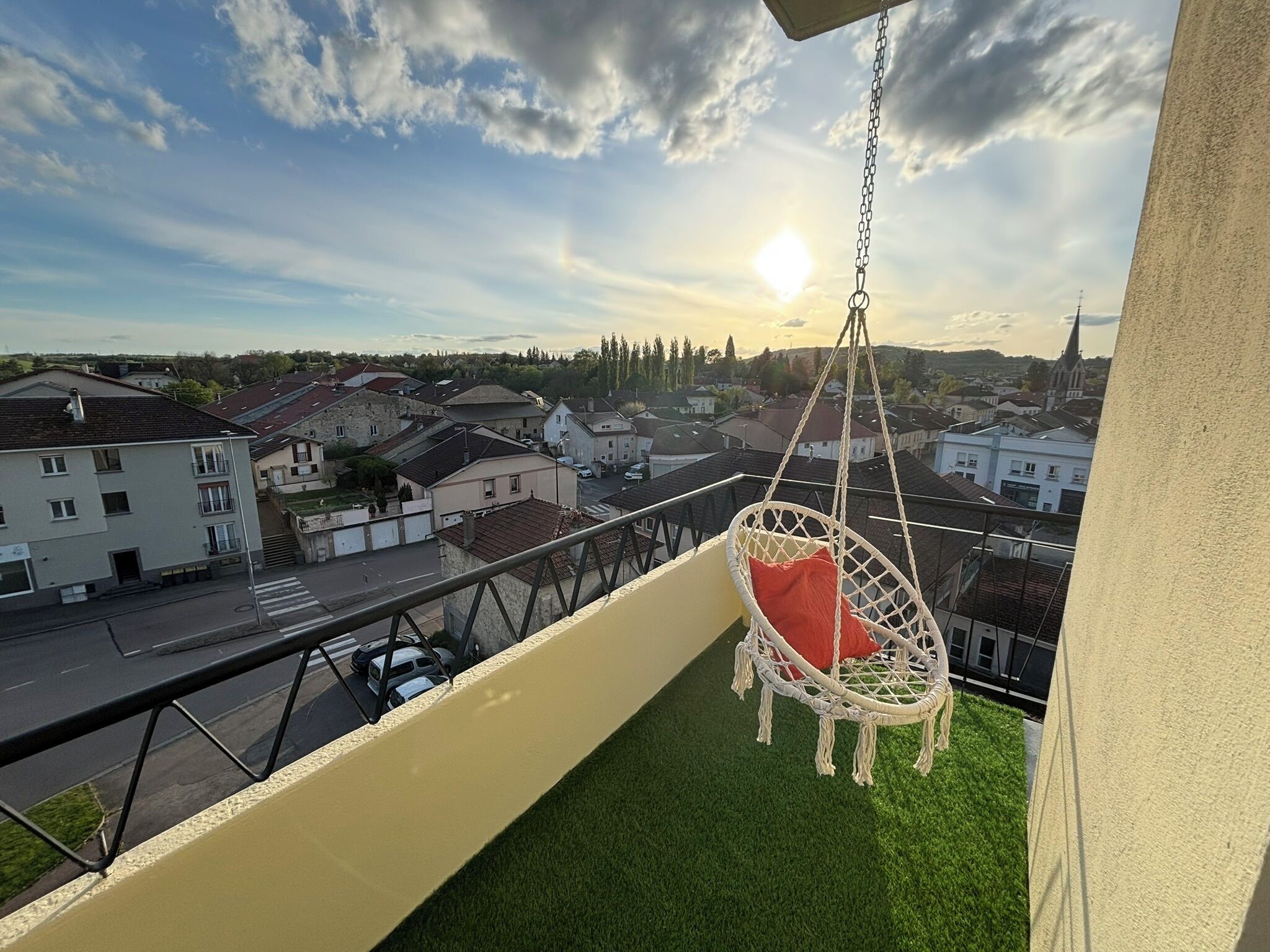 Un balcon avec un fauteuil suspendu, une vue sur la ville et un ciel dégagé.