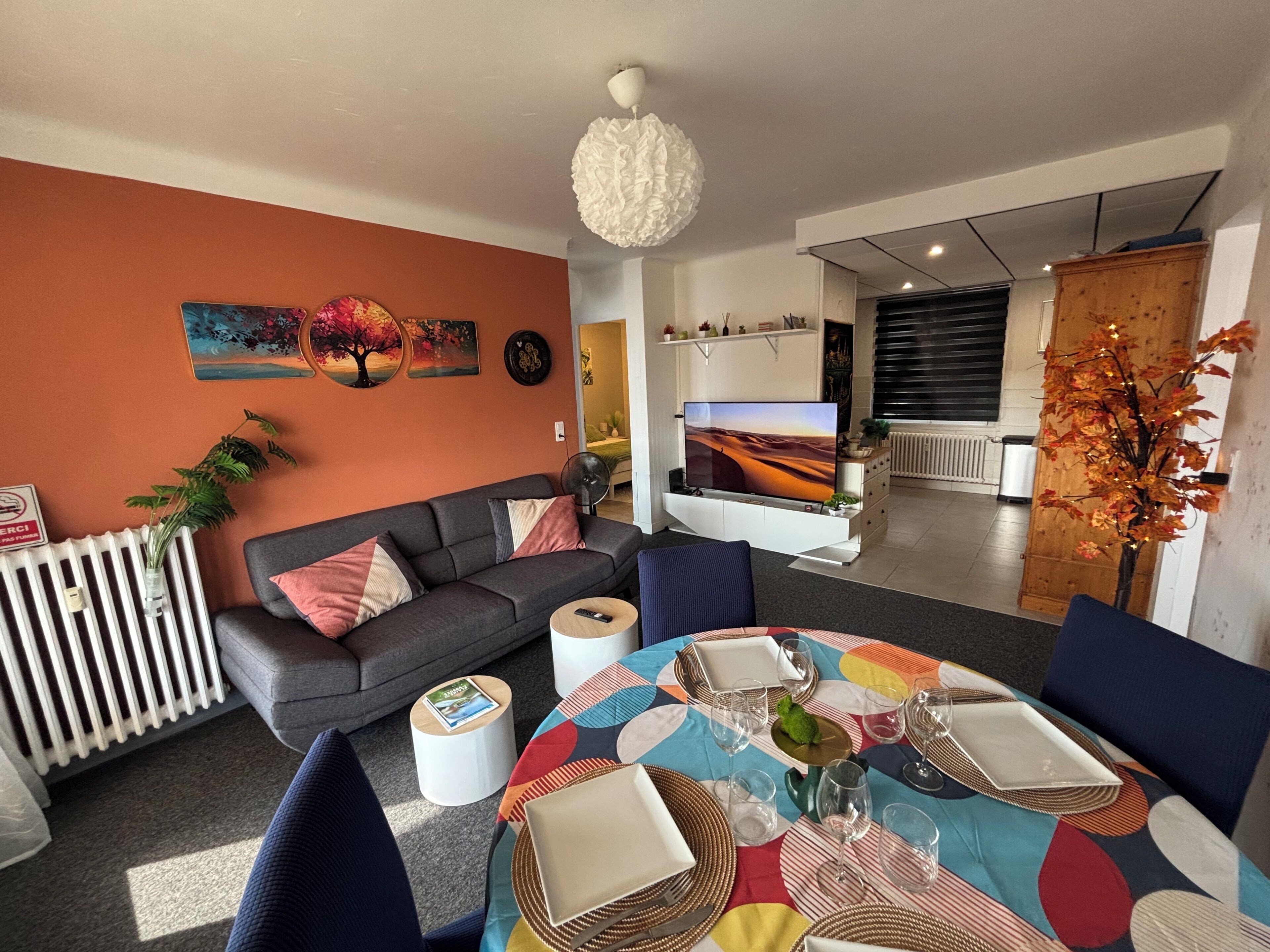 Una sala de estar con un sofá, una mesa de comedor preparada para cuatro personas y un televisor.