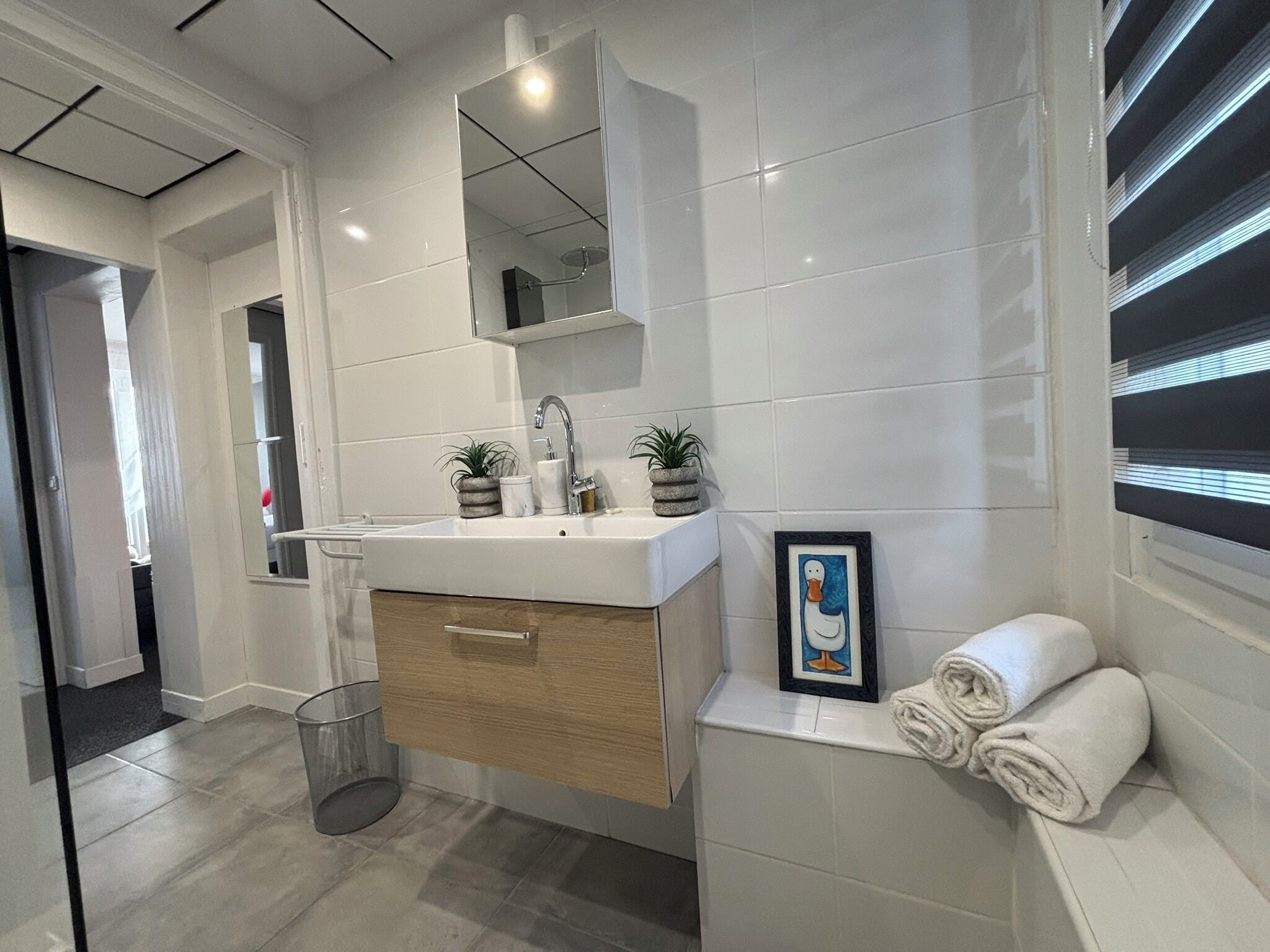 Une salle de bain moderne avec un lavabo blanc, un meuble en bois et un tableau encadré au mur.