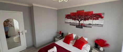 Een slaapkamer met een bed, nachtkastje, kunstwerk aan de muur en een plafondventilator.