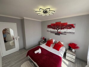 A bedroom with a bed, a nightstand, a wall-mounted artwork, and a ceiling fan. - Bright 75m2 3-bedroom Apartment with a largebalcony - fully equipped (Vittel)