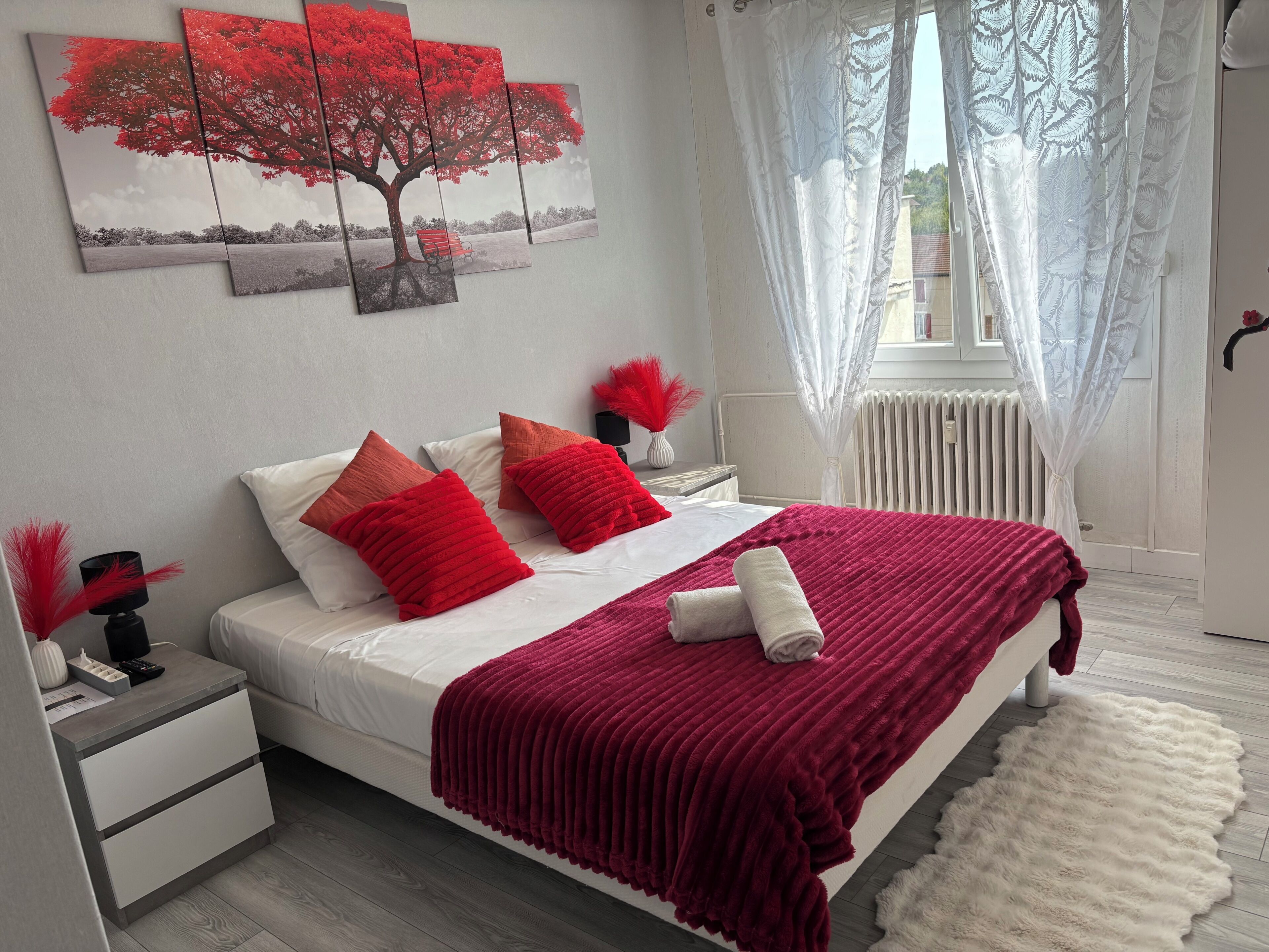 Une chambre moderne comprenant un lit, une table de chevet, une commode, une fenêtre avec des rideaux légers et une œuvre d’art accrochée au mur.