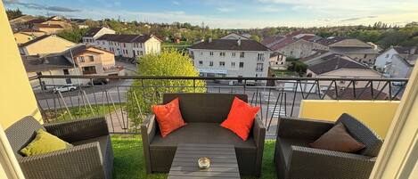 A balcony with wicker furniture, a small table, and a view of a residential area.