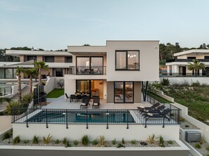 Une maison moderne à deux étages dotée d’une piscine, d’un espace salon extérieur et d’un balcon.