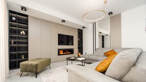 Een moderne woonkamer met een bank, poef, televisie, open haard en inbouwplanken.