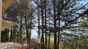 Ein Balkon mit Steinböden, einem Metallgeländer und Blick auf einen Wald und das Meer.