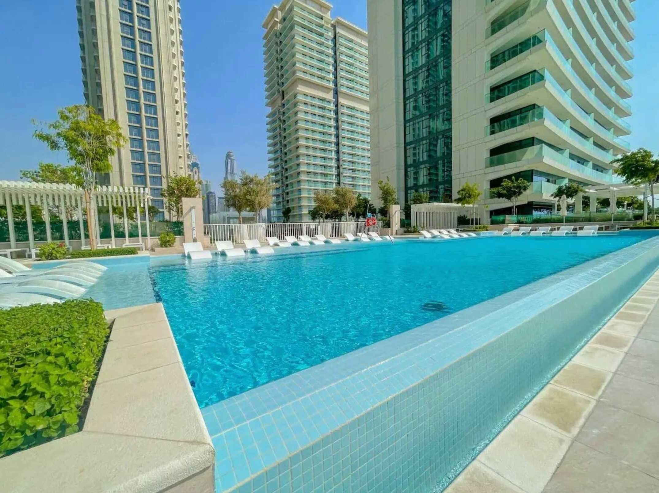 A swimming pool with lounge chairs, surrounded by high-rise buildings and greenery.
