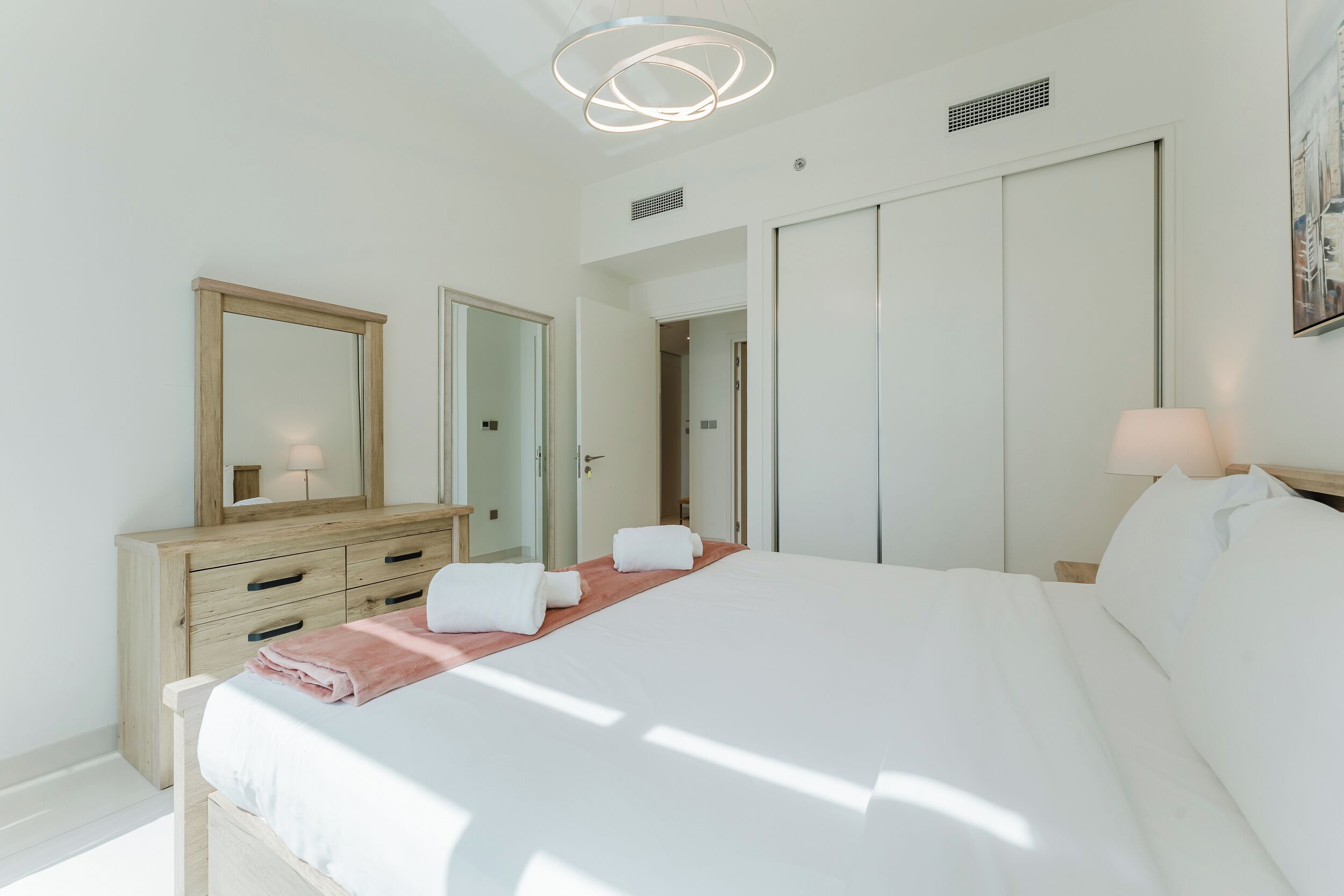 A bedroom with a bed, a dresser, a mirror, a door, and a wall-mounted light fixture.