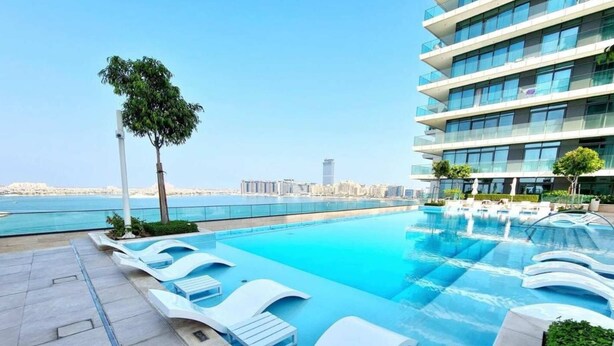En pool på taket med solstolar, fri utsikt över stadens silhuett och ett träd.
