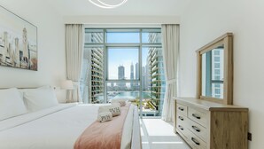Ett modernt hotellrum med en stor säng, en byrå i trä, ett stort fönster med utsikt över staden och en tavla på väggen.
