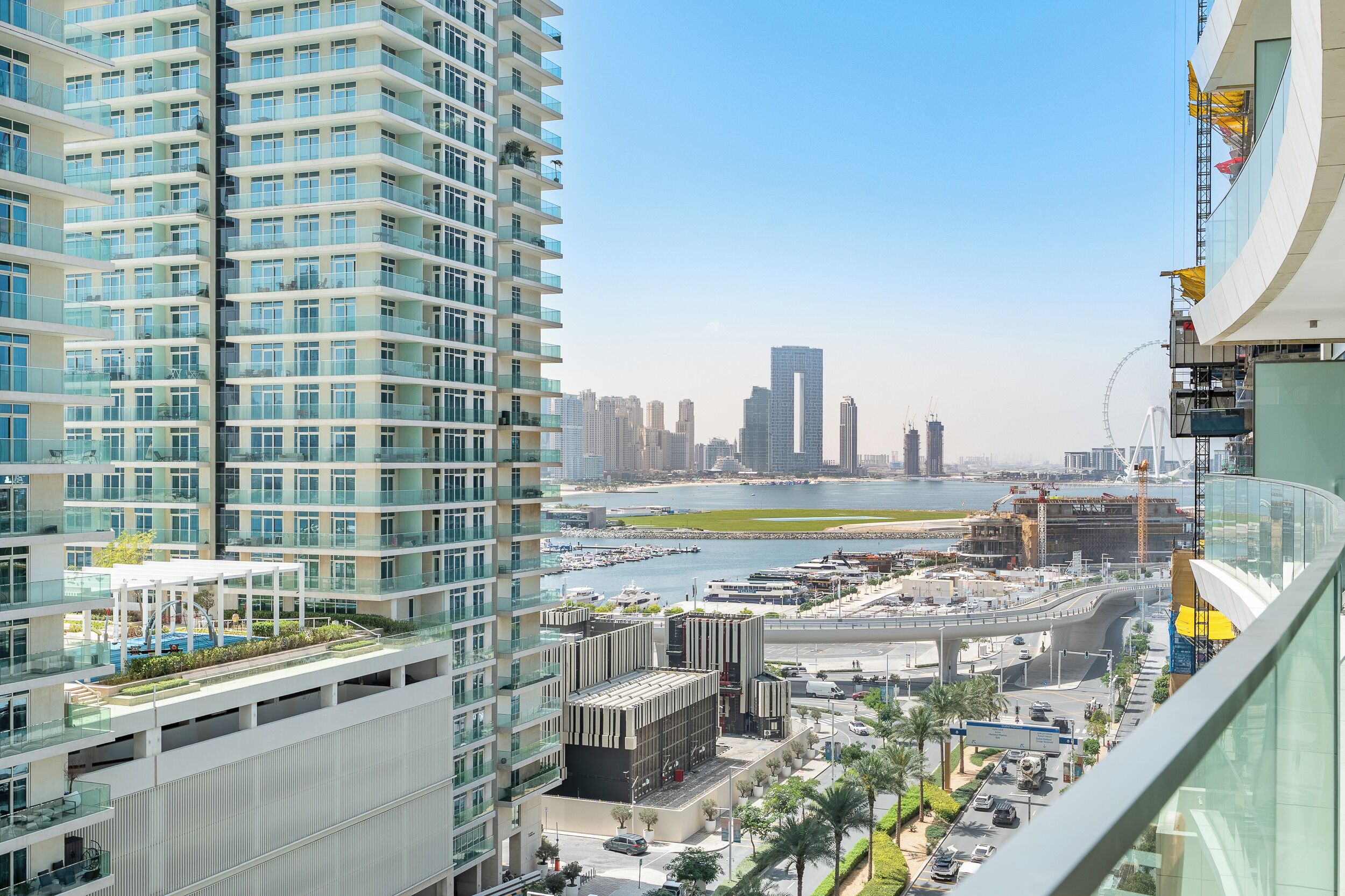 A high-rise building with multiple balconies, a marina with boats, and a clear view of the city skyline.