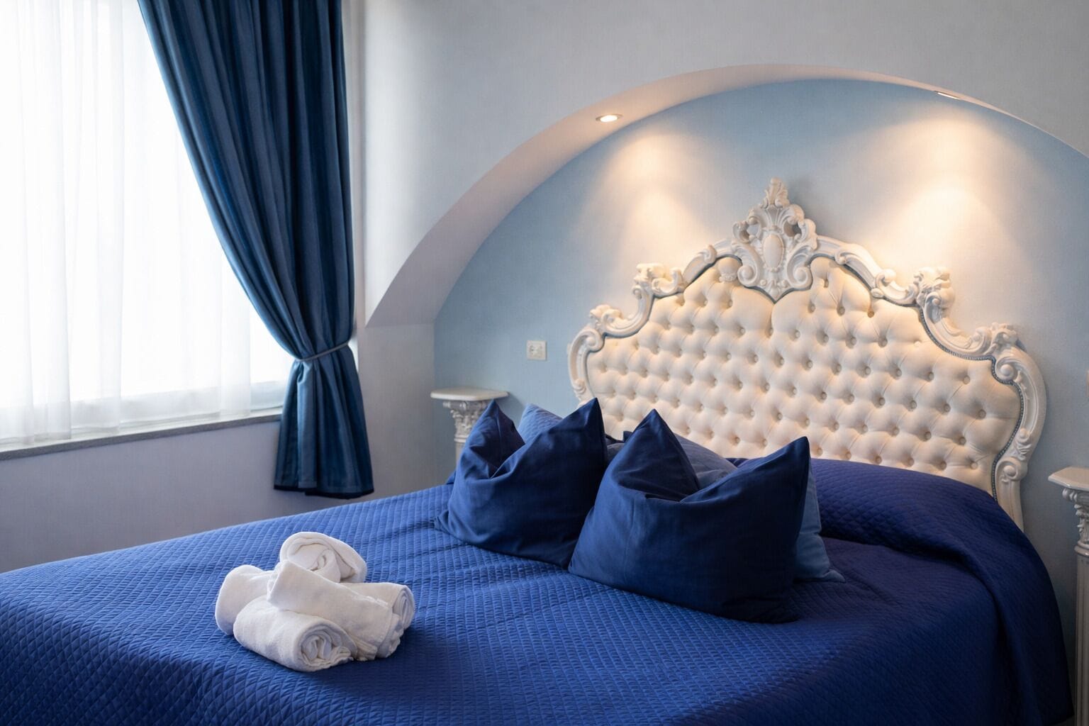 A bedroom with a tufted headboard, a blue bedspread, and dark blue pillows.