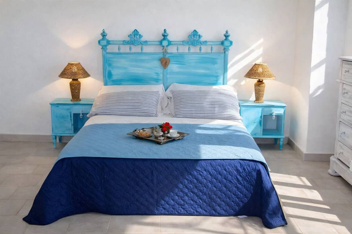 A bed with a blue headboard, two bedside tables with lamps, a tray with breakfast items, and a dresser.