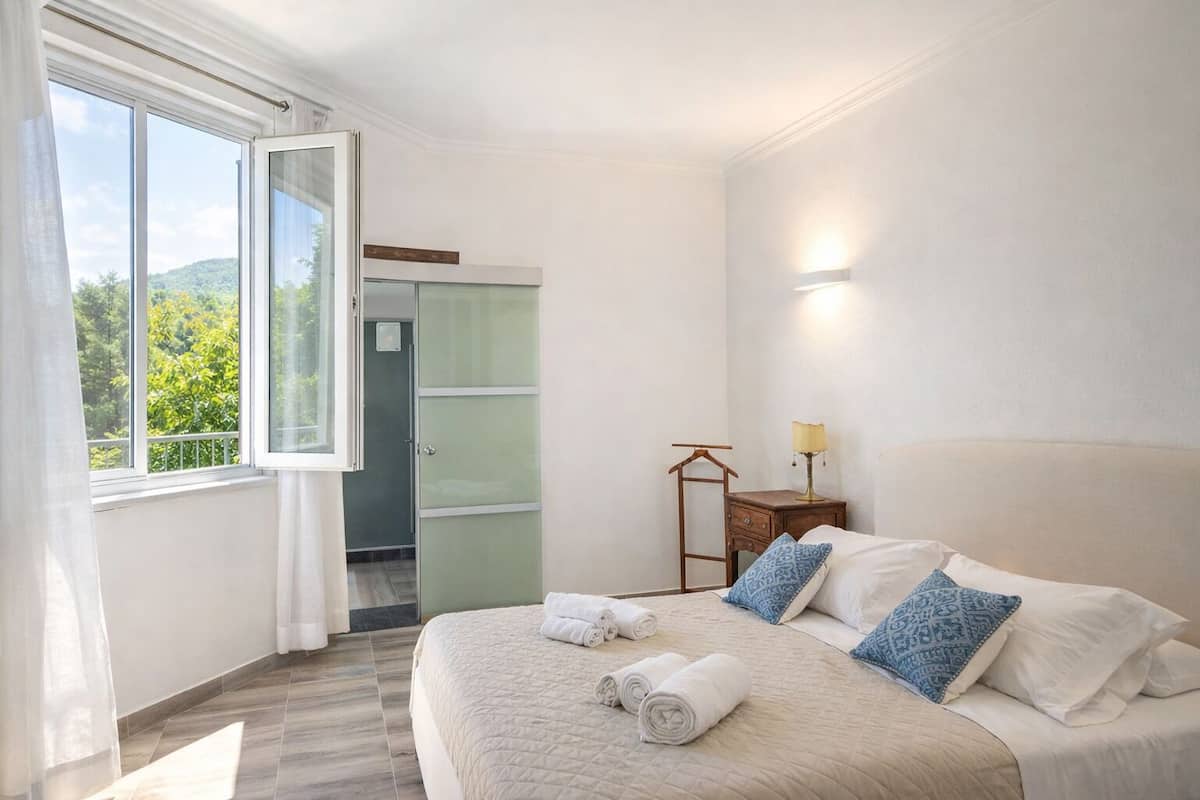 A bedroom with a bed, a nightstand, a lamp, and a window with curtains.