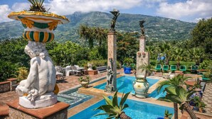 Zona de piscina con estatuas, una fuente y vistas a las montañas.