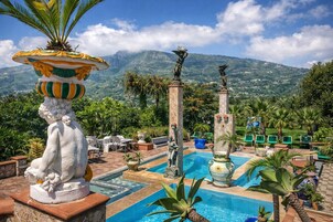 Zona de piscina con estatuas, una fuente y vistas a las montañas.