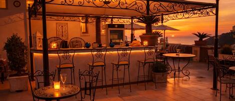 Une terrasse extérieure avec un bar, des chaises et des plantes en pot.