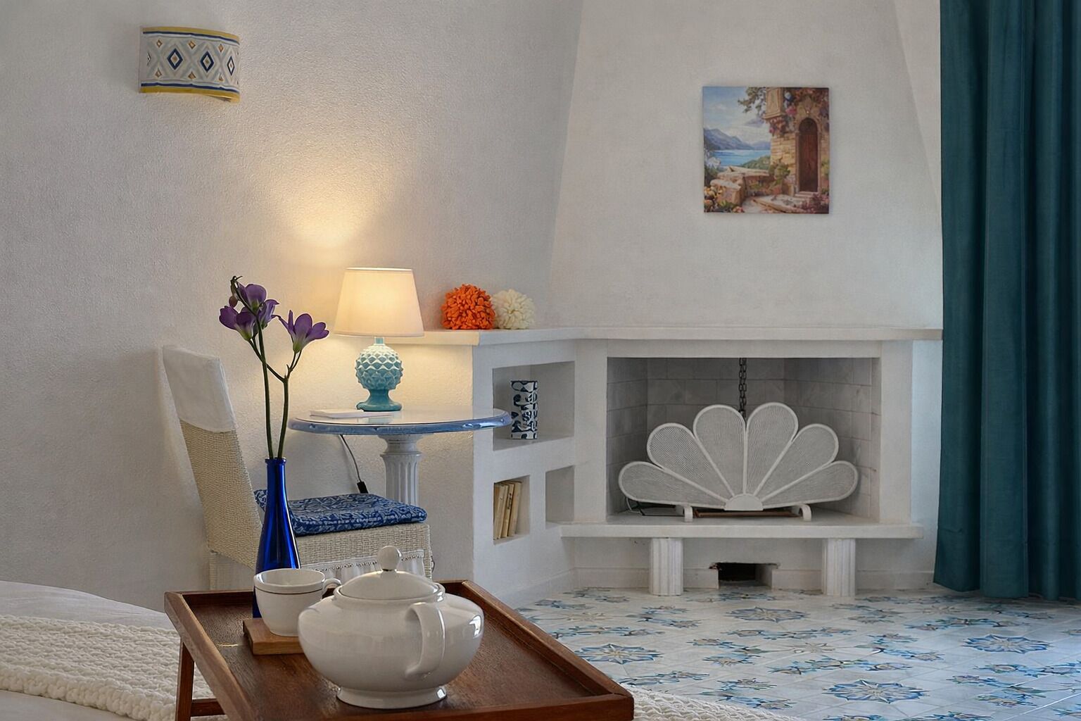 Une pièce avec une cheminée, une table sur laquelle se trouve un plateau, un vase rempli de fleurs et un tableau accroché au mur.