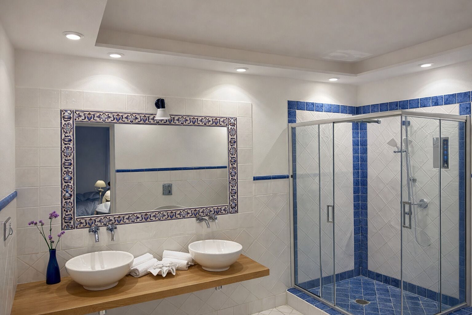 Un baño con dos lavamanos, un espejo grande y una ducha con mampara de cristal.