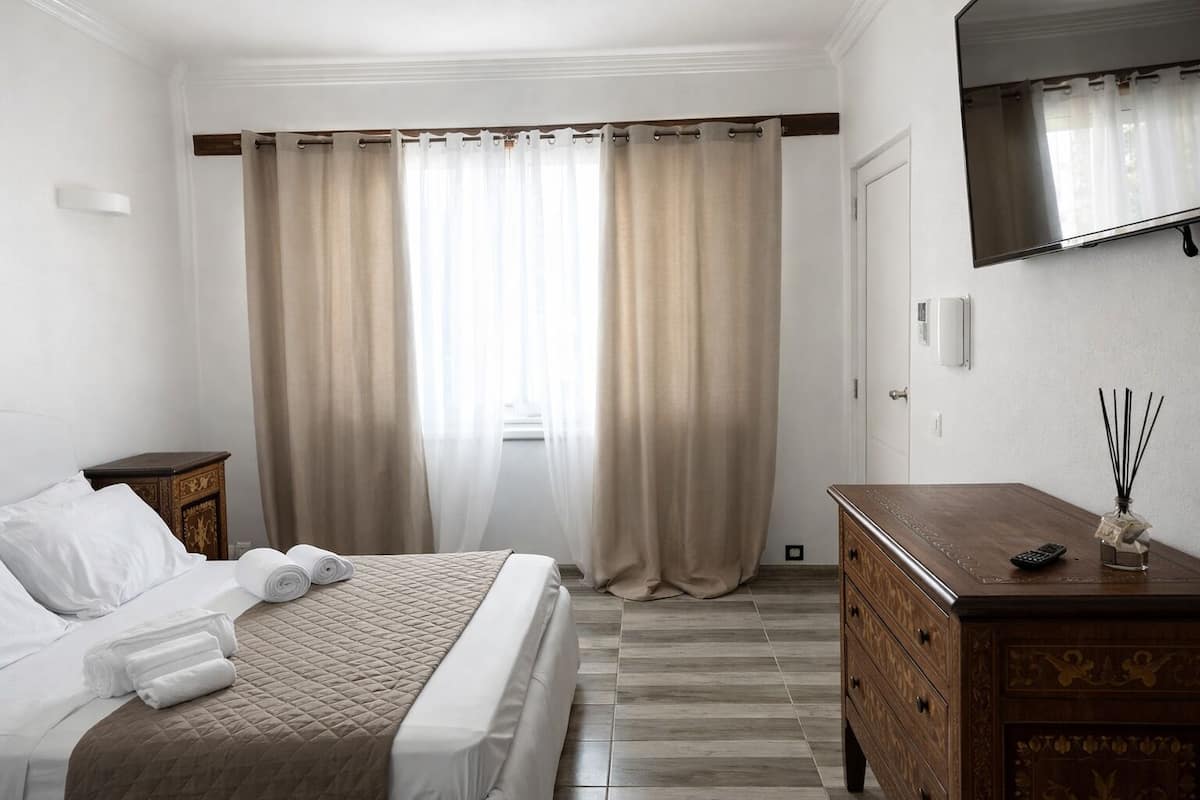 A hotel room with a bed, a wooden dresser, a mirror, and a window with curtains.