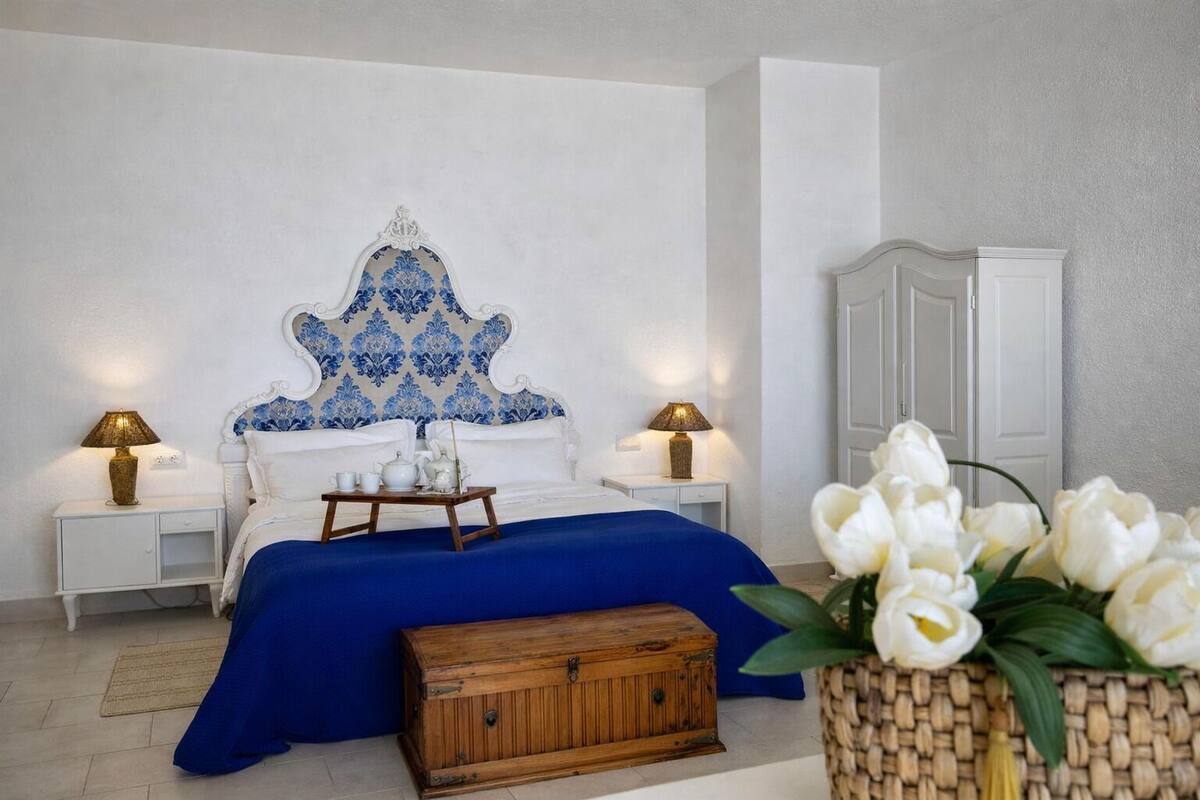 A bedroom with a bed, bedside tables, a wooden chest, and a vase of flowers.