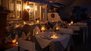Un área de comedor al aire libre con mesas dispuestas para una comida, iluminada con velas y faroles, bajo una estructura cubierta con ventanas.