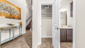 Un pasillo con una mesa consola de vidrio, un cuadro, una escalera, un armario y un baño con espejo y lavabo.