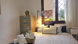 Un dormitorio con cama, mesita de noche, lámpara, ventana con vistas y cómoda.