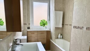 A modern bathroom with a white sink, a bathtub, and a window with a plant. - Apartment with large terrace - El Robledal 5925 (Isla)