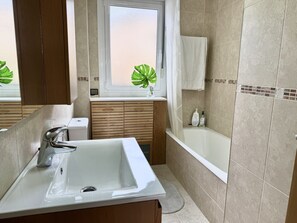 Ein modernes Badezimmer mit einem weißen Waschbecken, einer Badewanne und einem Fenster mit einer Pflanze.