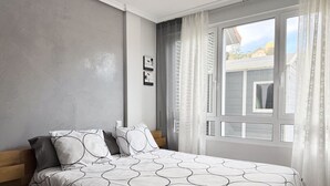 A bedroom with a bed, a nightstand, a window with curtains, and a view of buildings outside. - Apartment with large terrace - El Robledal 5925 (Isla)