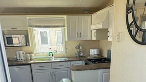 A compact kitchen with white cabinets, a microwave, a sink, a stove, and a trash bin. - 2 Bed - Sleeps 6 - Free Parking - Pets (Skegness)