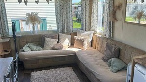 A cozy living area with a sectional sofa, a small table, and a window with curtains. - 2 Bed - Sleeps 6 - Free Parking - Pets (Skegness)