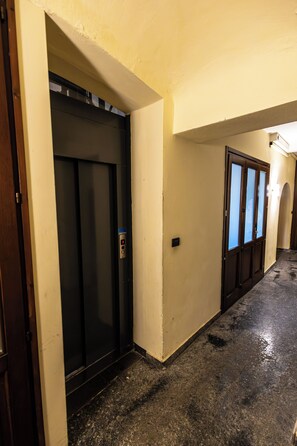 Un pasillo con ascensor, una puerta con paneles de vidrio esmerilado y suelo mojado.