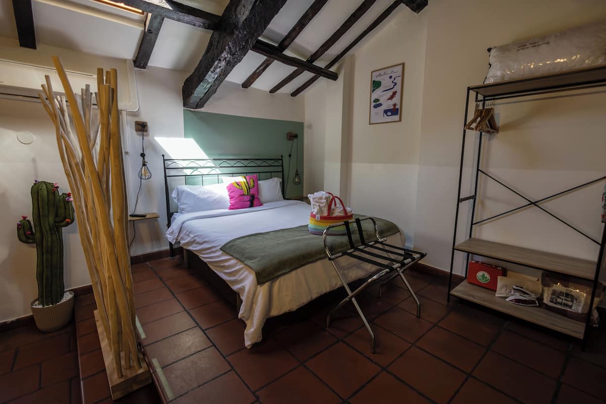Un dormitorio con cama, un tendedero de metal, un estante con objetos y una planta de cactus.