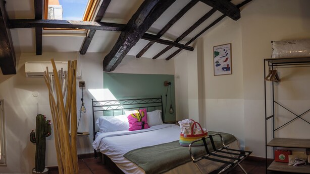 Een slaapkamer met een bed, een raam, een cactus, een metalen plank en een betegelde vloer.