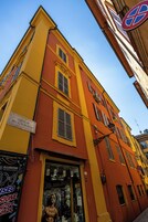 Rakennuksessa on keltainen julkisivu, myymälän sisäänkäynti ja kyltti, jossa lukee: ”VICOLLO DELL’ALBERGO”.