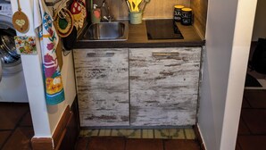 Een compacte keuken met een rustiek houten kastje, een spoelbak en diverse keukengerei.