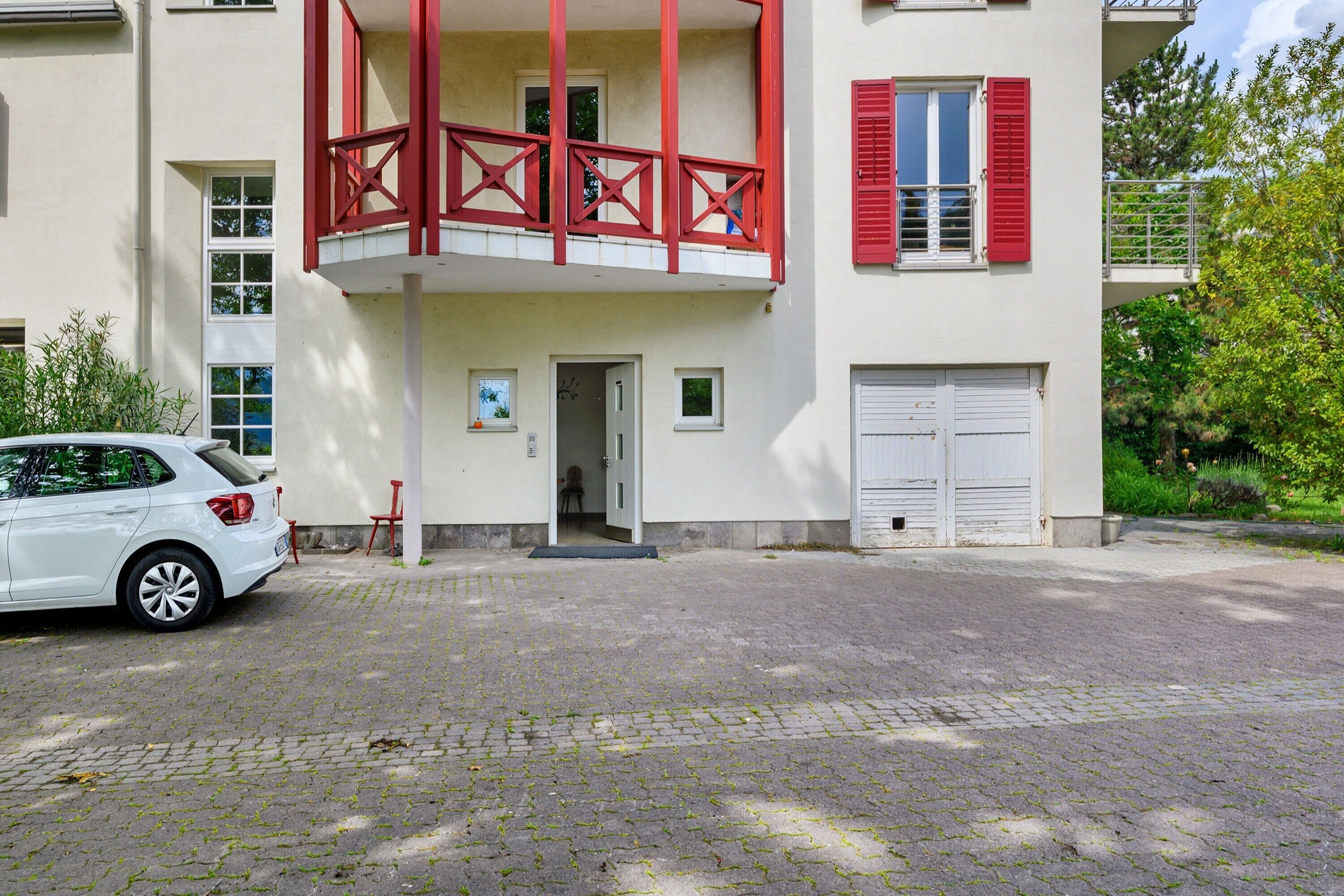 A building with a red balcony, a white car parked in front, and a door leading to the entrance.