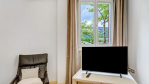 Una habitación con una silla reclinable, un televisor de pantalla plana sobre un soporte de madera y una ventana con cortinas.