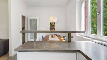 Une cuisine moderne dotée d’un long comptoir, d’une table à manger avec des chaises, d’un luminaire suspendu et d’une fenêtre donnant sur un paysage verdoyant.