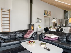 Ein modernes Wohnzimmer mit Kamin, schwarzen Ledersofas, einem Couchtisch und einem Essbereich mit Tisch und Stühlen.