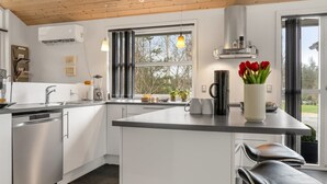 Una cucina moderna con mobili bianchi, un lavello in acciaio inossidabile, una macchina per il caffè e un vaso con tulipani rossi.