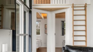 Un interno moderno con un divano in pelle nera, una scala in legno e vista su una camera da letto attraverso una porta aperta.