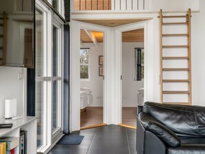 Ein modernes Interieur mit einem schwarzen Ledersofa, einer Holzlade und Blick durch eine offene Tür auf ein Schlafzimmer.