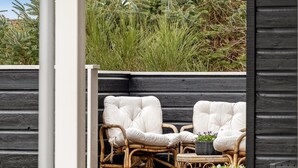 Un patio con sedie in vimini e un tavolino, circondato da un pavimento in legno e una recinzione nera.