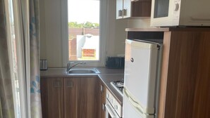 A compact kitchen with wooden cabinets, a built-in microwave, a refrigerator, and a window with a view of the outside. - El Palmar Paradise . (El palmar, Vejer de la frontera)