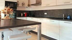 A modern kitchen with white cabinets, a dark countertop, and a bar area with stools. - L'Écrin d'Olmo: Charming & spacious terrace in a peaceful setting (Pietrosella)